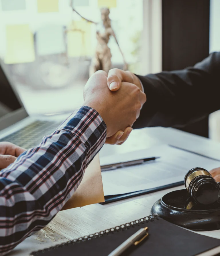 Apretón de manos entre abogado y cliente sobre un escritorio con documentos legales.