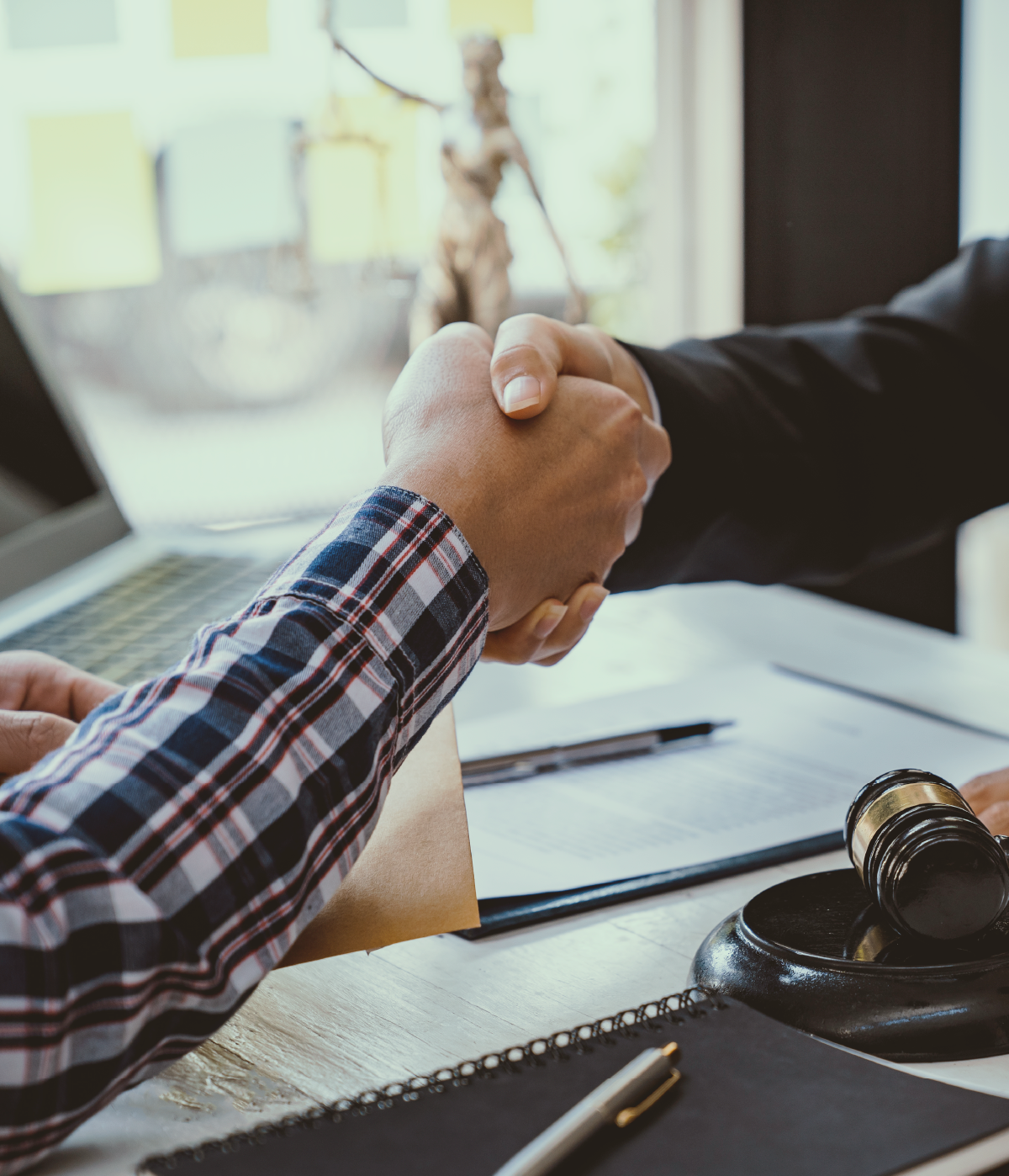 Apretón de manos entre abogado y cliente sobre un escritorio con documentos legales.