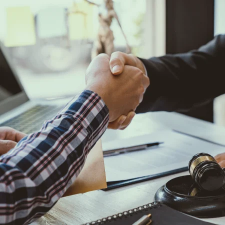 Apretón de manos entre abogado y cliente sobre un escritorio con documentos legales.